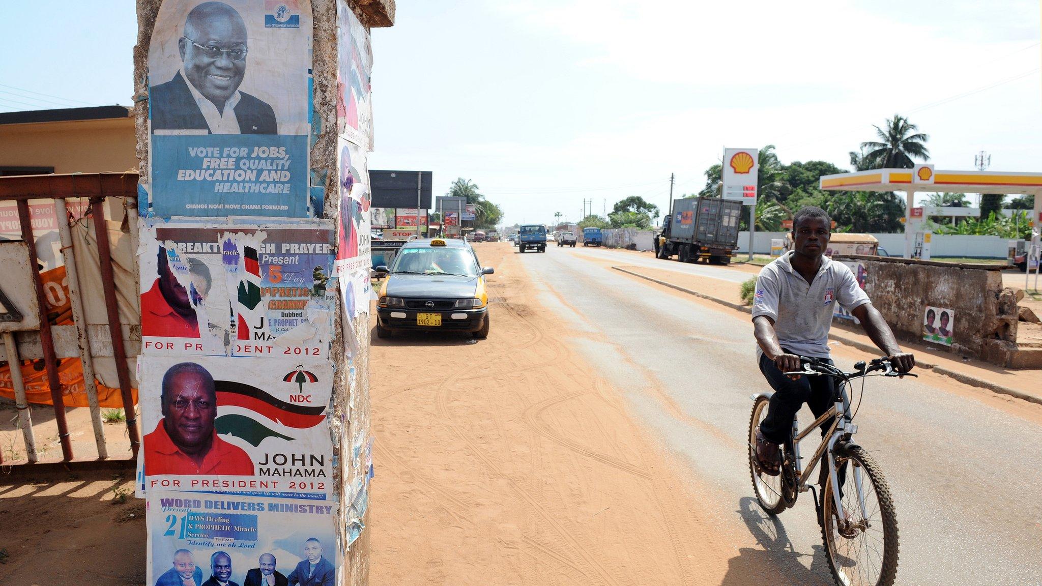 Man in Ghana cycles past presidential election posters featuring President John Dramani Mahama and his main challenger, Nana Addo Dankwa Akufo-Addo, on 23 October 2012