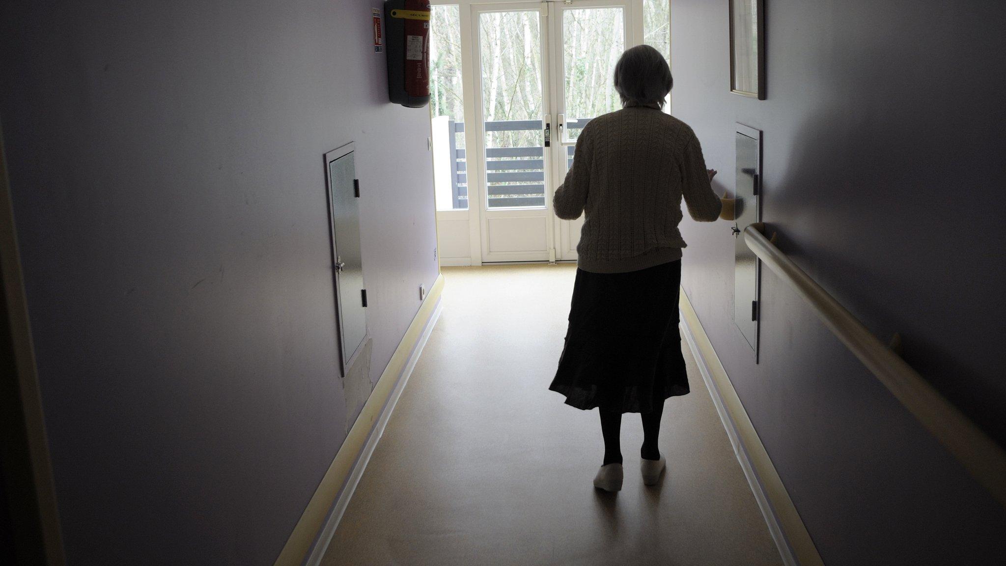 A dementia sufferer walks down a care home corridor.