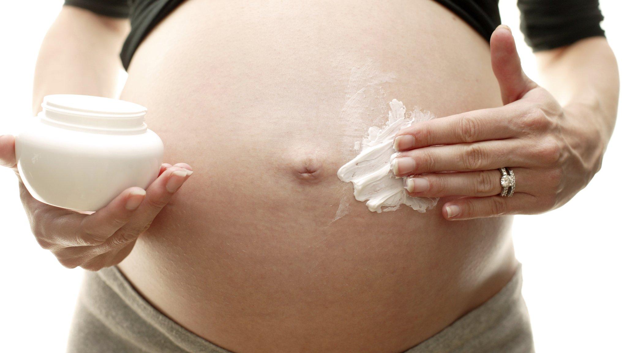 pregnant woman applying moisturiser to her bump