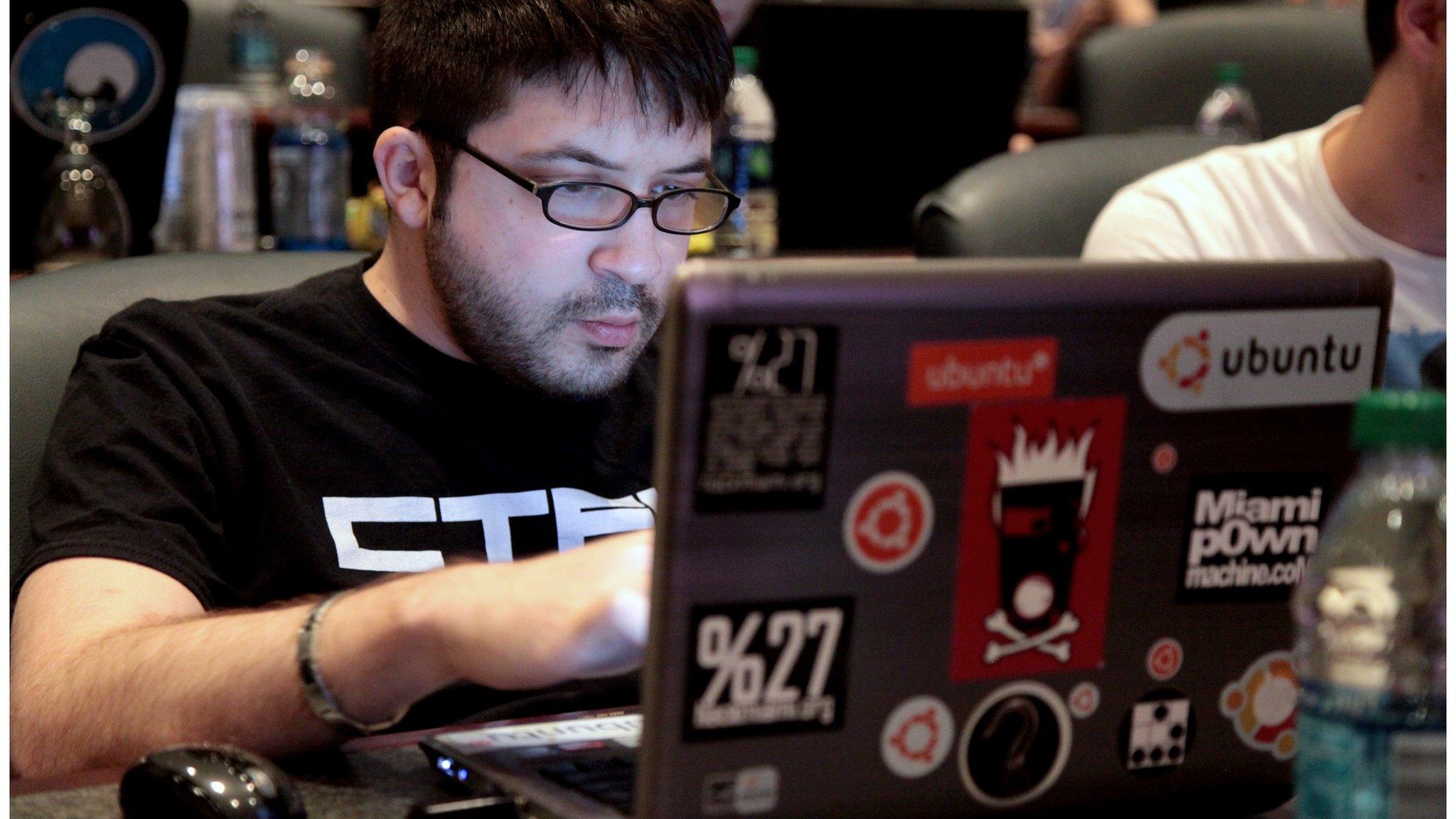 A man behind a computer covered in stickers