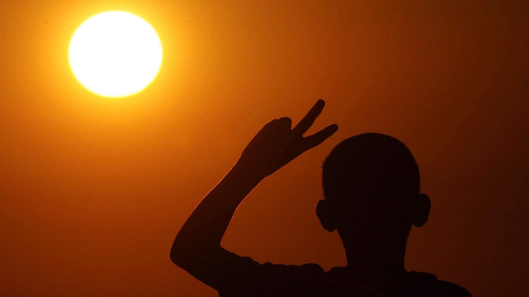 A boy flashes a victory sign amid the backdrop of a rising sun