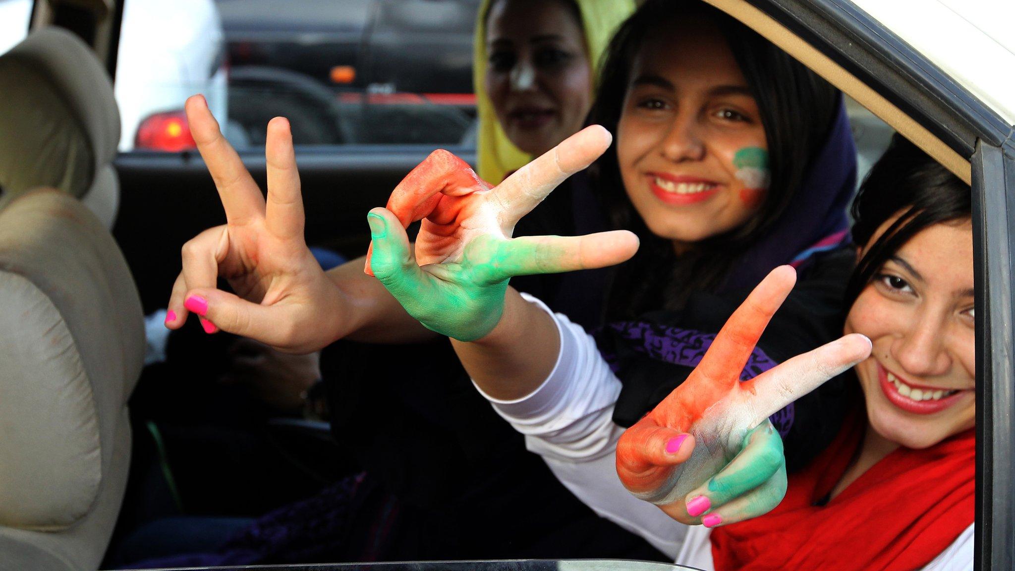 Three Iranian women football supporters in a car with their hands and faces painted in the colours of Iran's flag