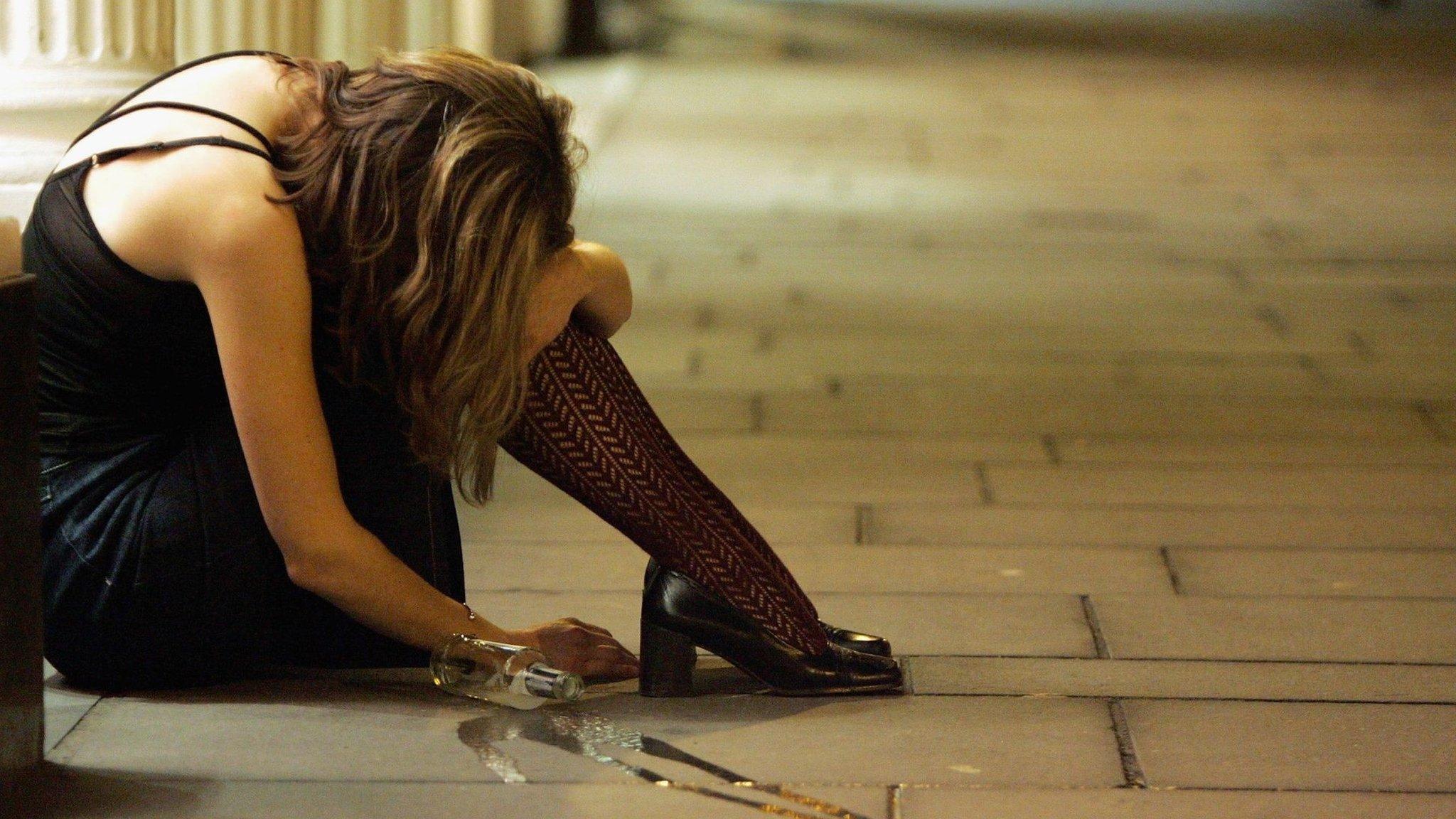 Woman slumped on pavement with a spilt bottle beside her