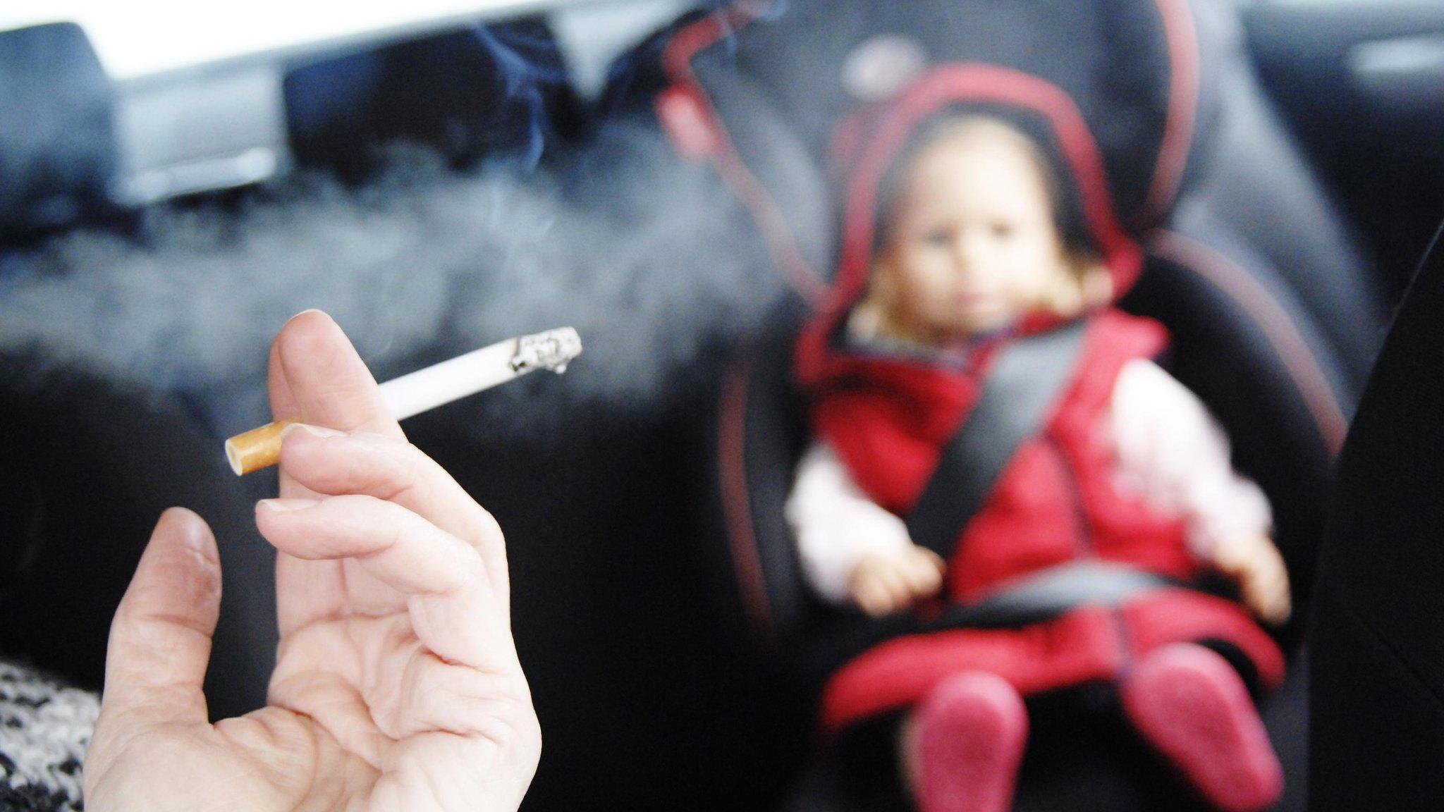 Person smoking in car with a small child in the back seat