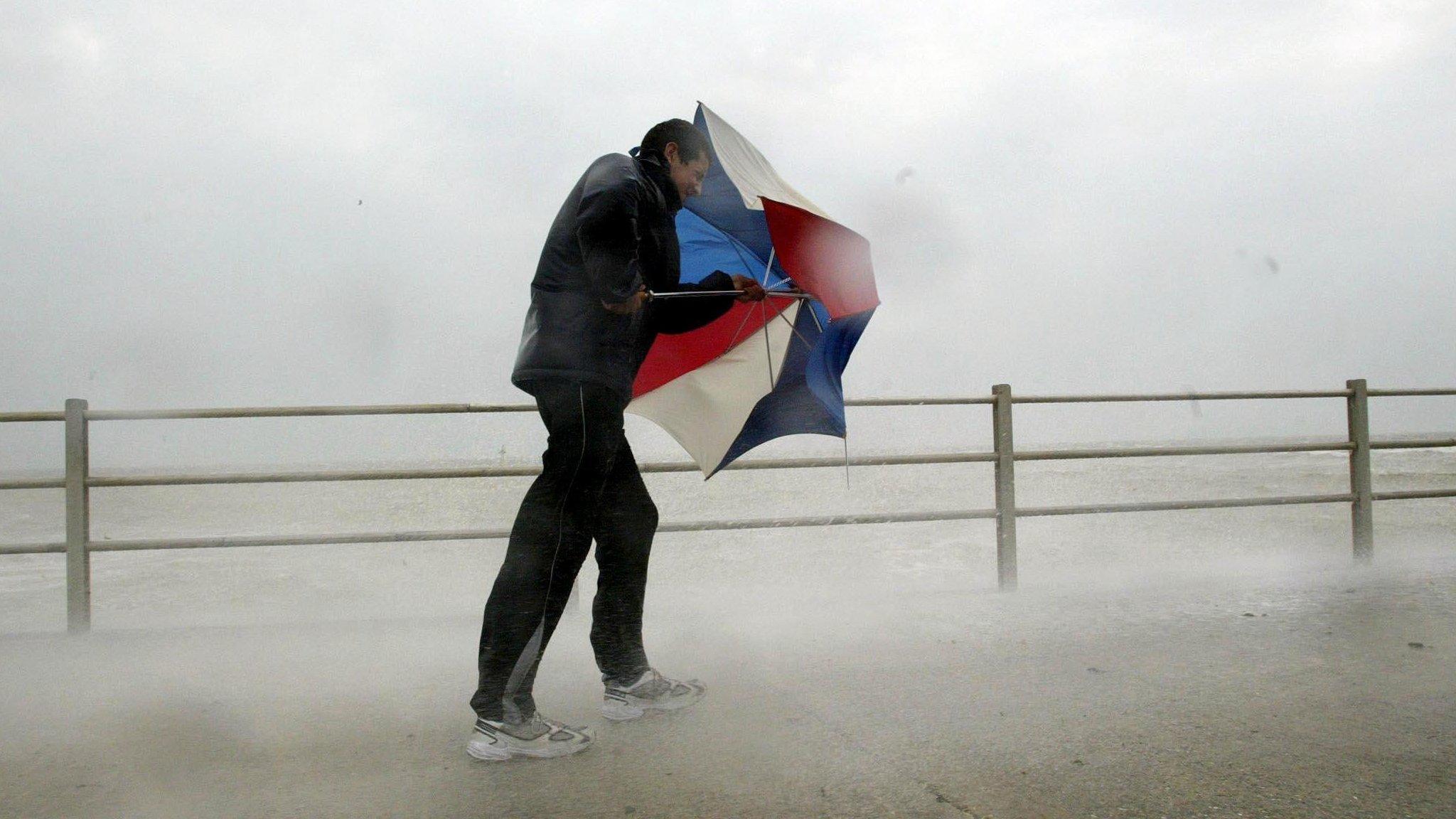 Man with umbrella battling the elements on the seafront