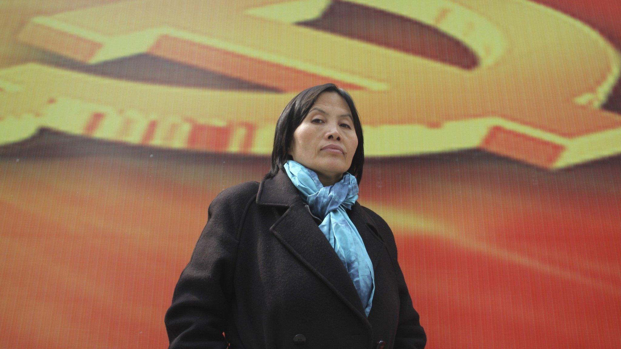 Prominent Chinese human rights activist Cao Shunli stands in front of an emblem of the Chinese Communist Party during an interview in the central business district of Beijing March 23, 2013