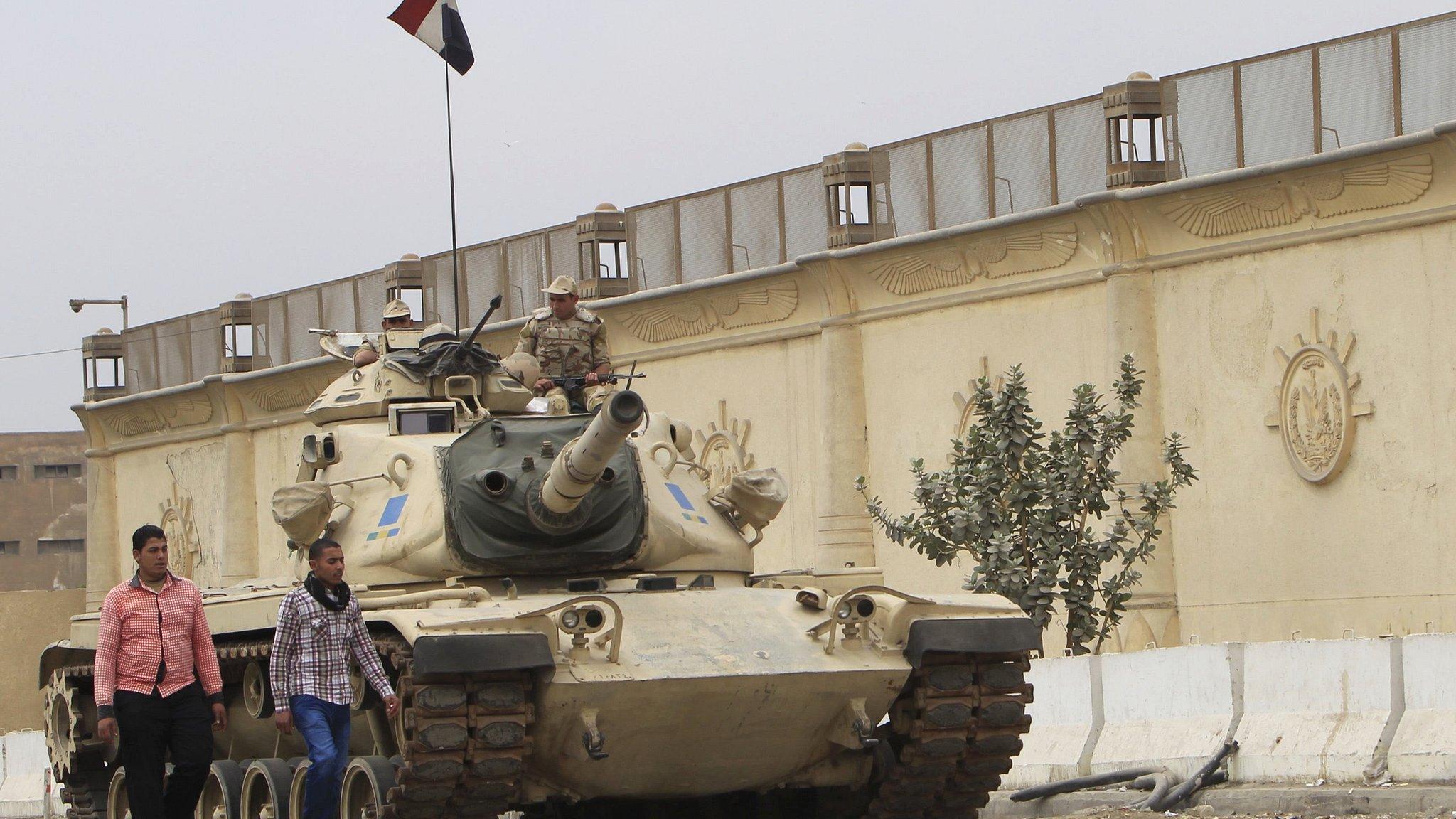 People walk past an Egyptian army tank positioned outside Cairo's Tora prison on 23 March 2014