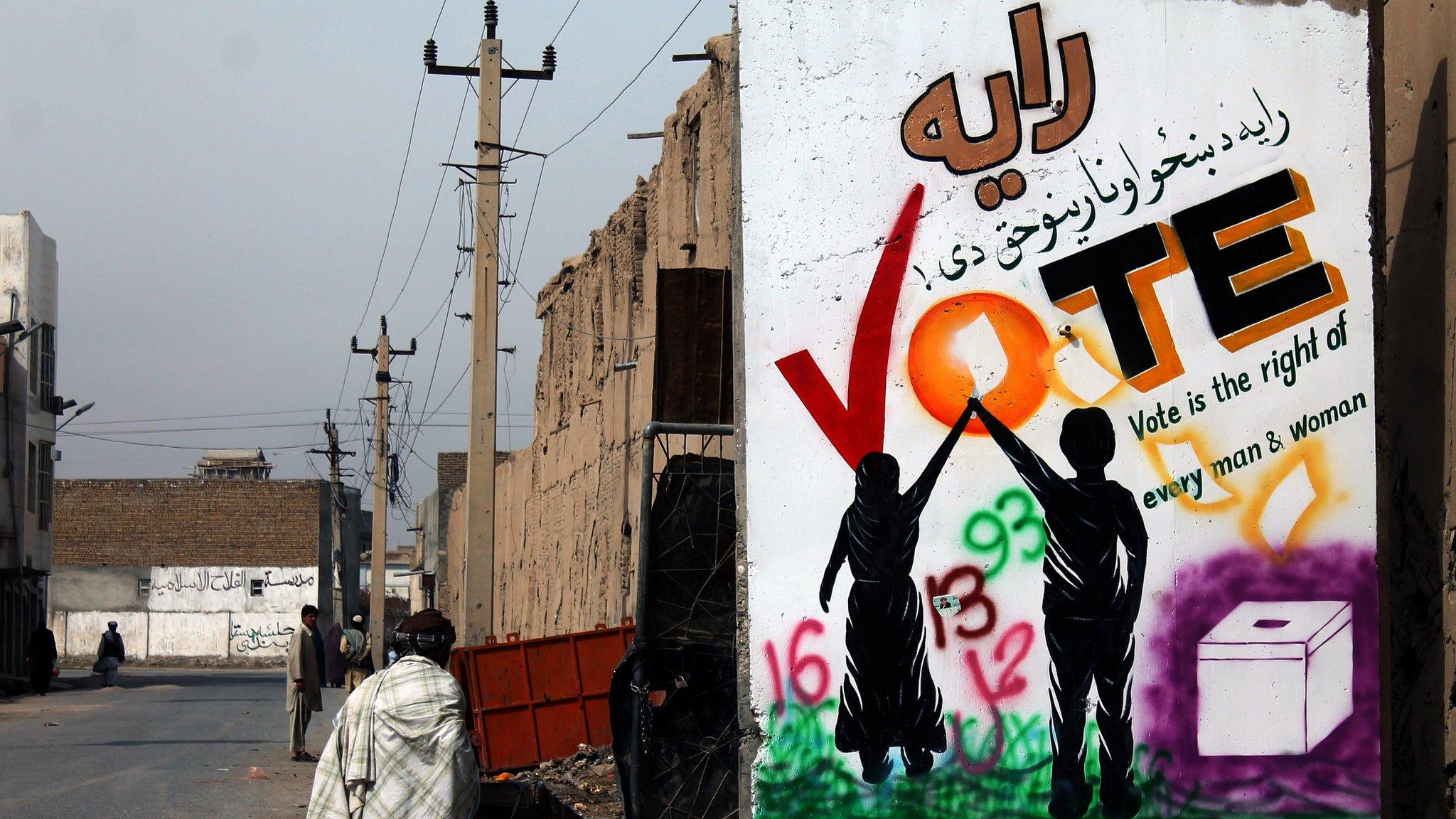 An Afghan pedestrian walks past a wall decorated with an election mural in Kandahar