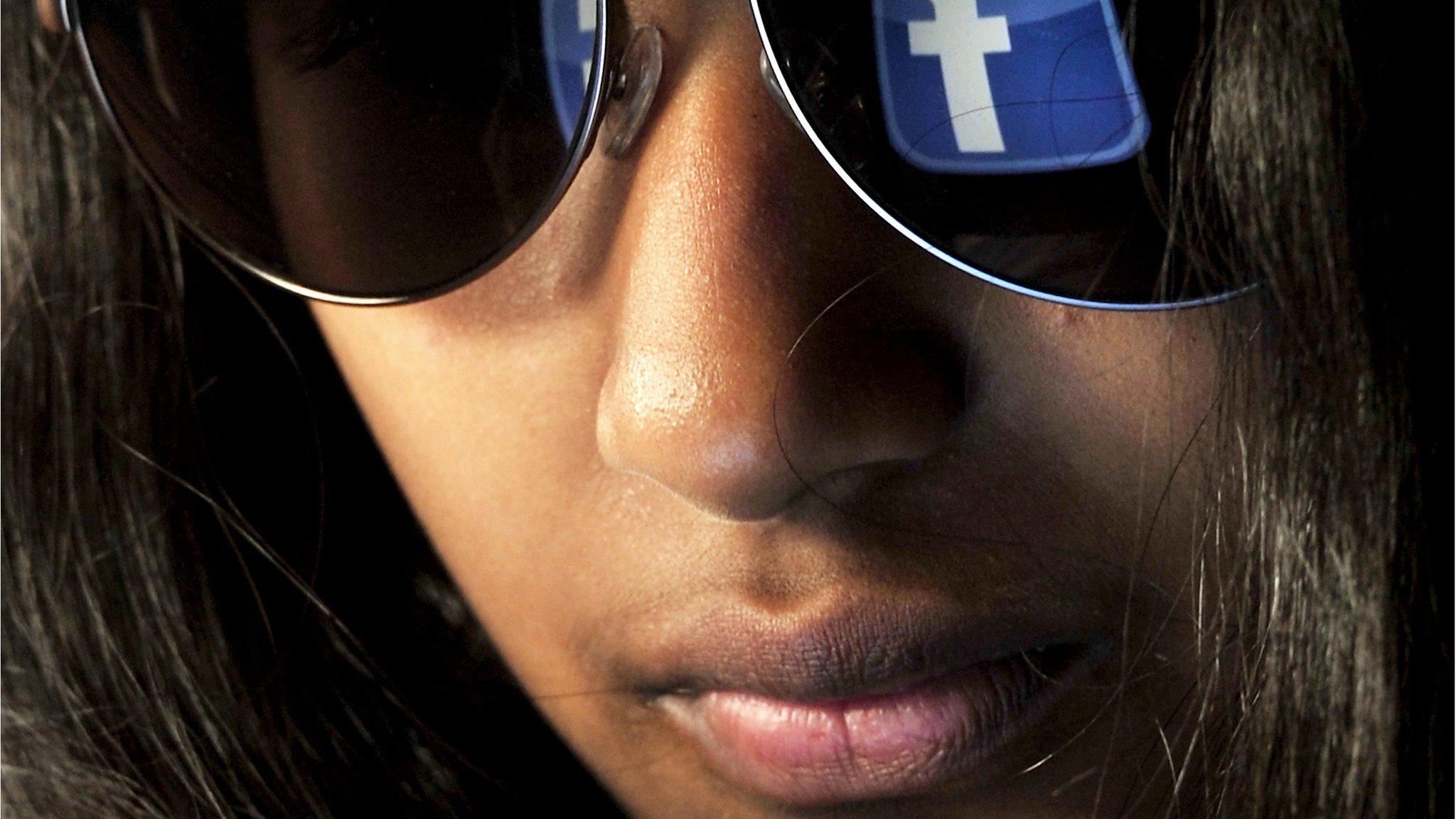 A woman with the Facebook logo reflected on her sunglasses