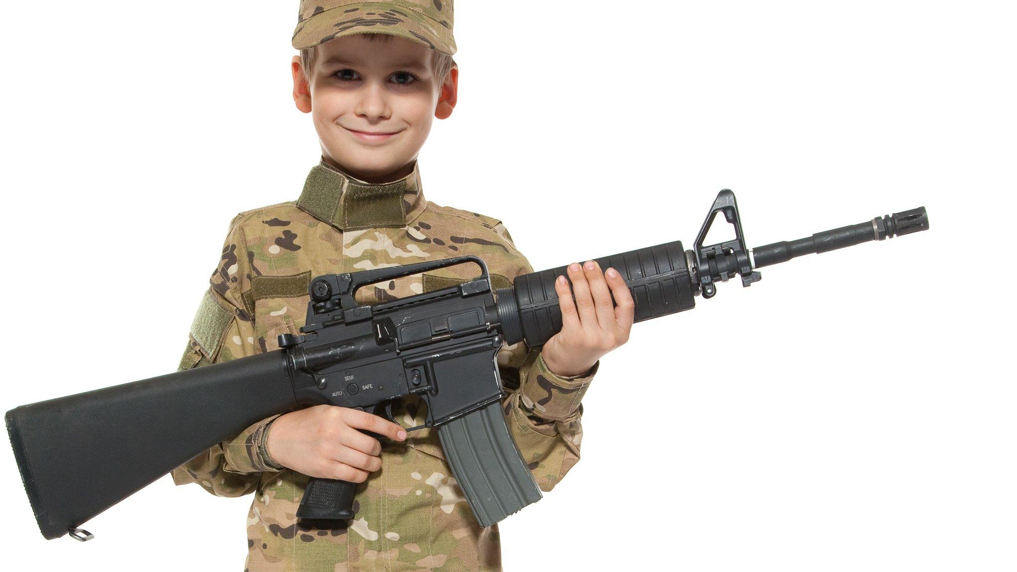 A young boy dressed as a soldier poses with a large gun