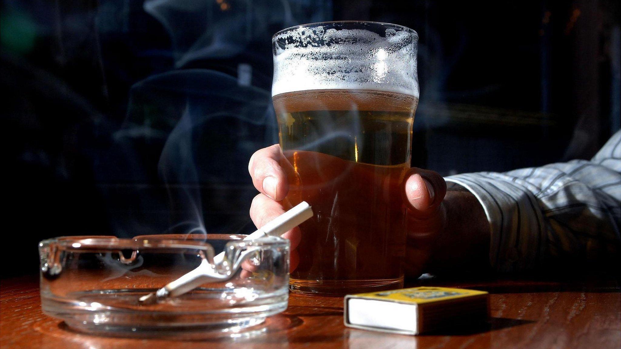 Man holding pint of beer and lit cigarette in ashtray