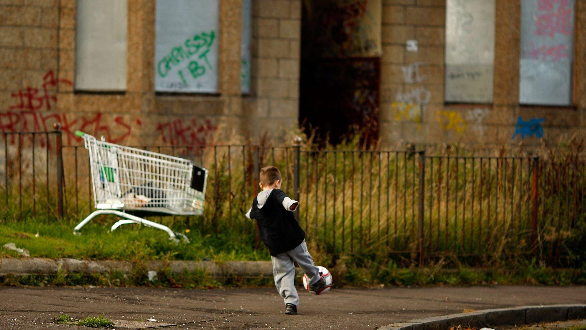 Child playing football in front of boarded up homes