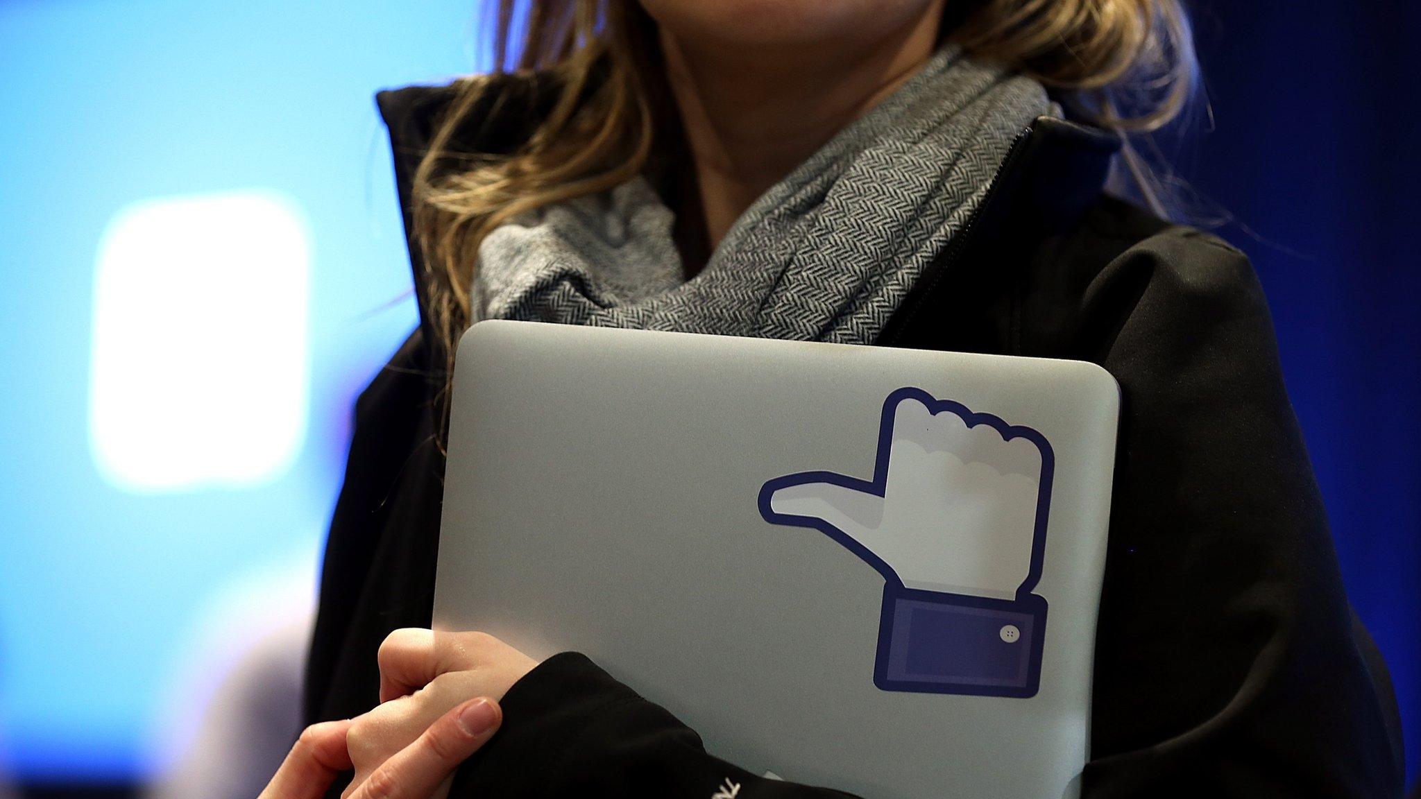 Woman holds laptop with thumbs-up 'like' logo