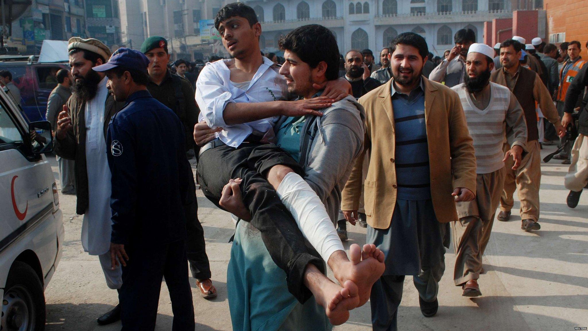 A man carries an injured student following a gun attack in Peshawar