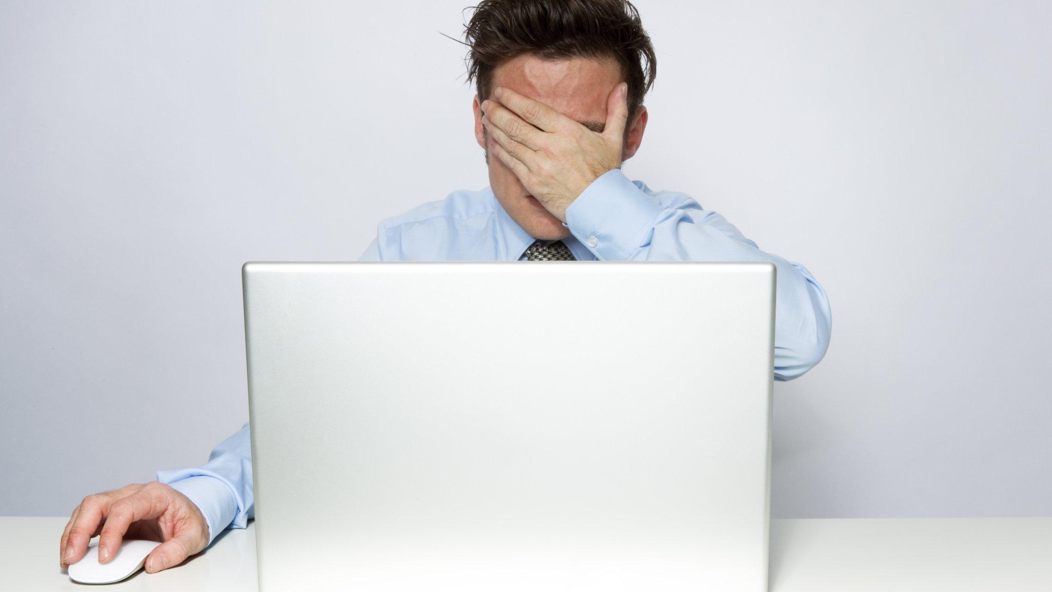 Man by computer with hand over eyes