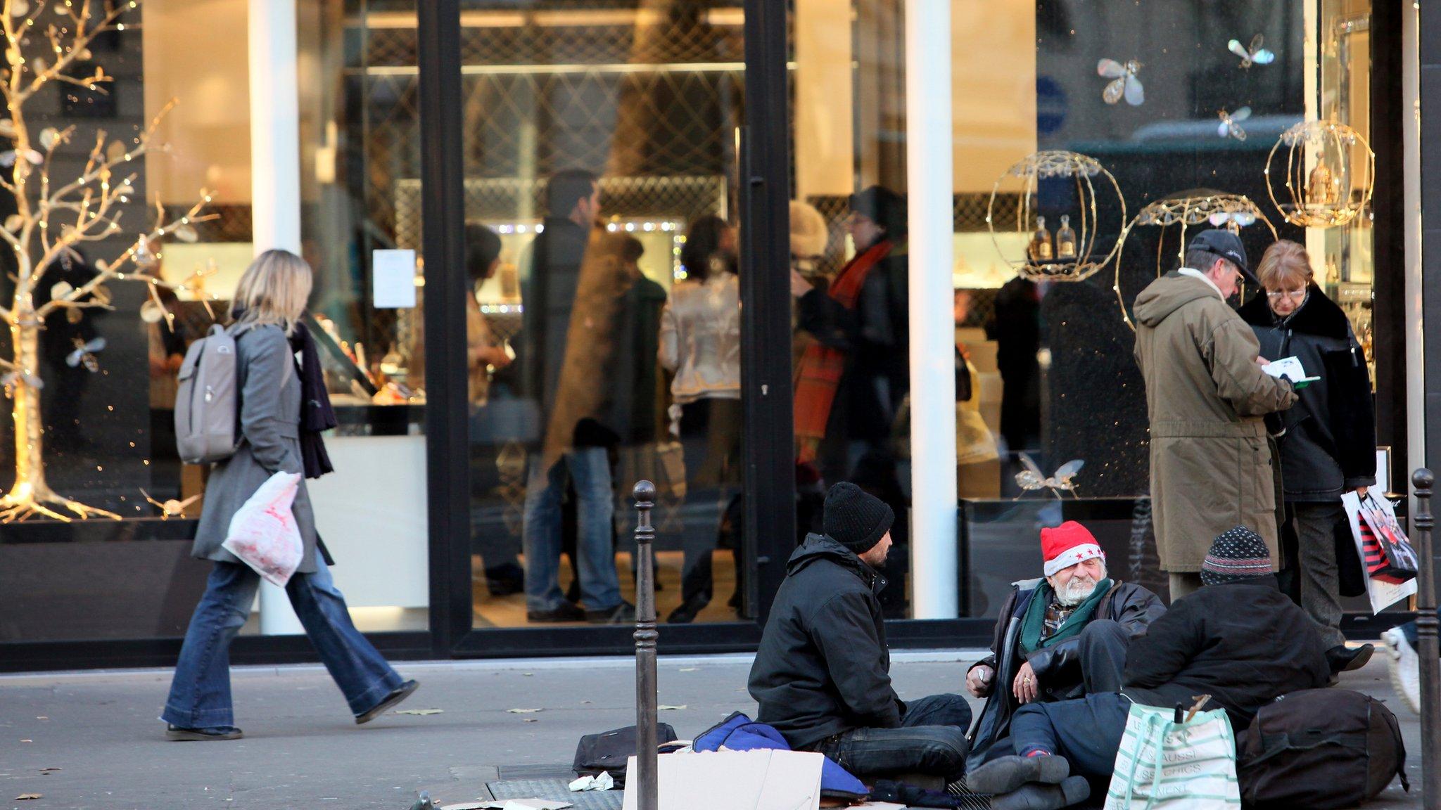 Homeless people beg in a street next to a luxury store in Paris