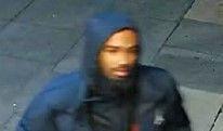 CCTV image of a man wearing a dark blue jacket with the hood up and pavement in the background