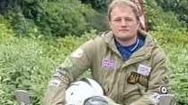 A photograph of a man on a scooter dressed in a green Mod jacket and navy polo shirt 