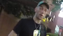 Another view of the same man, taken from a slightly underneath angle. In this picture he is looking directly at the camera, and appears to be saying something. The background is badly pixelated. 