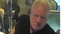 A grainy CCTV image of a bald man wearing a black T-shirt on a train.
