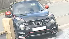 A CCTV image of a black Nissan Juke with red wing mirrors driving along a street.