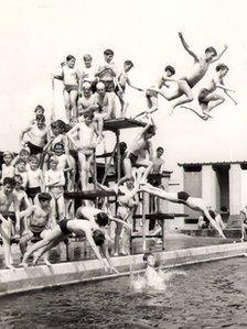 A black and white photo of boys jumping off the diving board