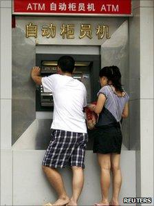 A man and a woman use an ATM machine located outside a bank in central Beijing