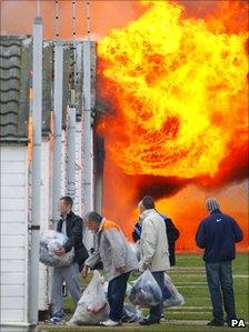 Prisoners carry bags into a jail building as flames engulf part of the compound