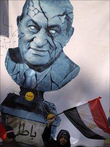 An Egyptian girl waves a national flag beneath a picture of a cracked bust of Egypt's President Hosni Mubarak with Arabic writing below reading "invalid", Cairo, Egypt, 11 February 2011
