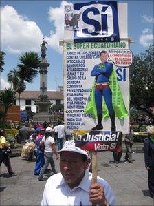 Luis Simba carries a placard with an image of Rafael Correa as a superhero