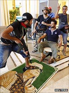 A former rebel steps on a poster of Col Muammar Gaddafi while others pose for the camera at the Rixos Hotel in Tripoli