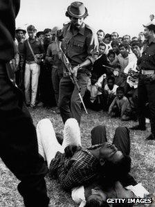 A Mukti Bahini guerrilla about to bayonet men accused of collaboration with Pakistan during Bangladesh's war of independence, at a racecourse in Dhaka, 1971