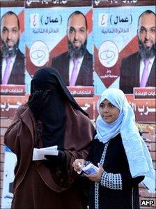 An Egyptian woman wearing a full face veil and a girl stand by campaign posters for a candidate from al-Nur