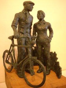 Miniature model of a statue showing man pushing a bike alongside a woman