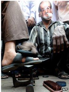 A cobbler wearing a mask of controversial British author Salman Rushdie polishes shoes outside a mosque during a protest by an Islamic organisation in Mumbai on January 11, 2011