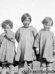 Two mixed-race children stand either side of an Inuit