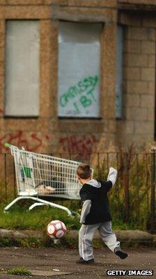 Boy kicking football by a boarded up house