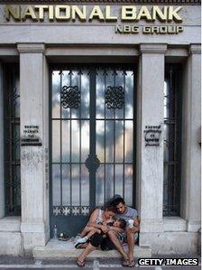 A family beg on the street in front of the offices of National Bank on June 14, 2012 in Athens, Greece.