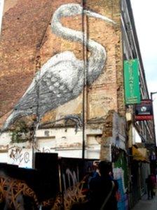 Tourist taking a photograph of Roa's crane just off Brick Lane