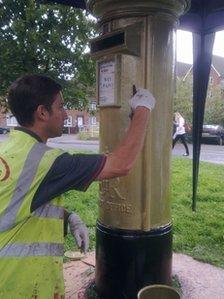 A contract worker painting the postbox in Alton gold for Royal Mail