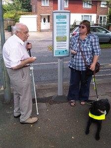 Two people using a talking bus stop