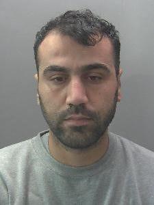 A police photograph of a dark-haired man with a dark beard wearing a round-necked grey T-shirt.