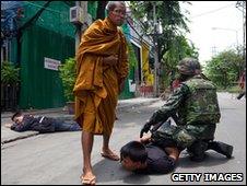 A monk watches a soldier detain a protester in Bangkok on 19 May 2010