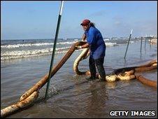 A BP clean-up worker stretches an oil-soaked boom along a beach on Elmer's Island, Louisiana, 23 May