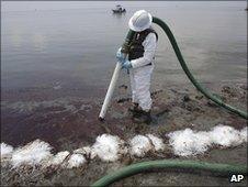 A worker uses a suction hose to remove oil washed ashore in Belle Terre, Louisiana