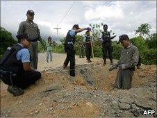 Thai bomb squad members inspect the crater at the site of a roadside bomb