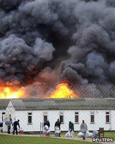 Inmates carry their possessions and walk from burning buildings during a riot at Ford open Prison, near Arundel, on 1 January 2011