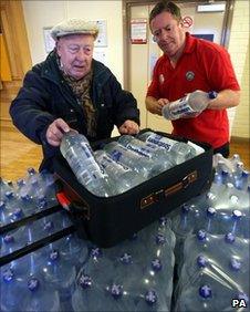 Elderly man packing water bottles into suitcase