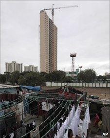 In this Nov. 9, 2010 file photo, an Indian laundry worker hangs clothes to dry on his terrace with the backdrop of the 31-story Adarsh Housing Society apartments in Mumbai, India.