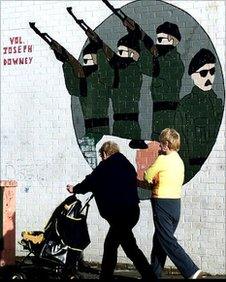 Two women pushing pram past paramilitary mural